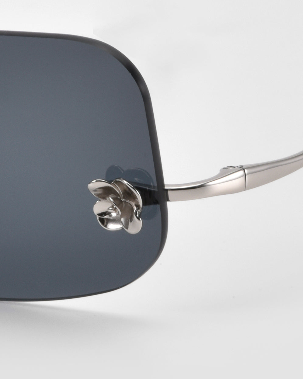 Close-up of For Art's Sake® Magnolia sunglasses, featuring dark tinted lenses, a silver metal frame, and floral-shaped nose pads against a white background.
