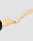 Close-up of the gold, wavy temple arm on For Art’s Sake® Abstraction I sculptural metal sunglasses, displayed against a light gray background.