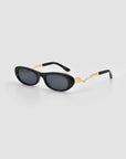 Abstraction I by For Art's Sake®: black oval sculptural metal sunglasses with dark lenses and gold accents on the arms, shown against a light gray background.
