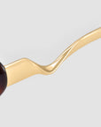 Close-up of Abstraction I sunglasses by For Art's Sake® featuring a gold, wavy sculptural metal temple arm, set against a light gray background.