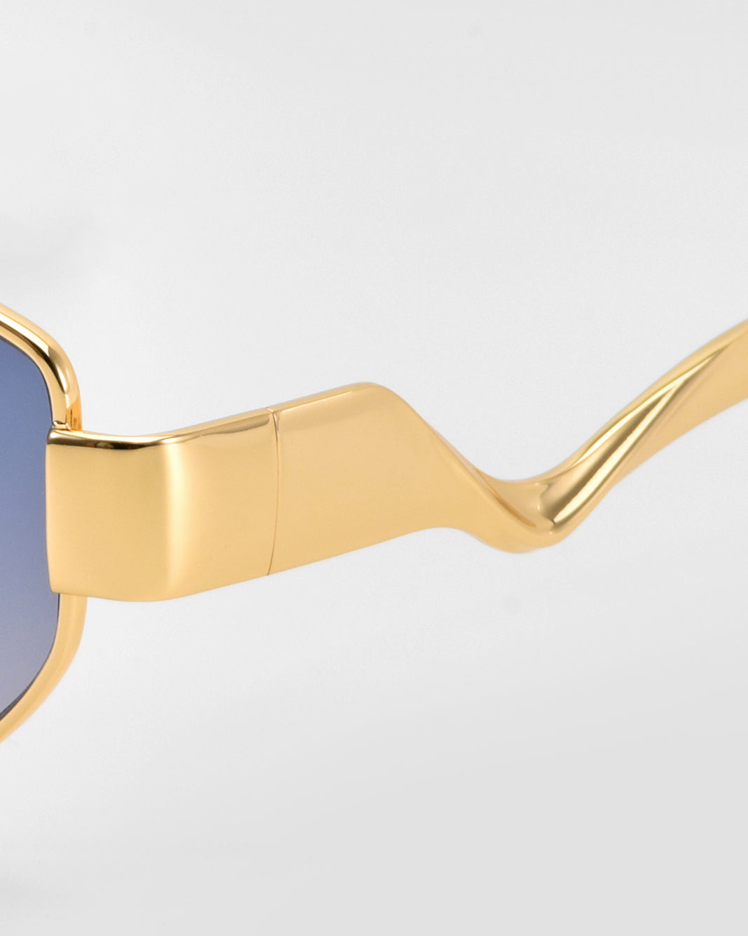 Close-up of Abstraction II by For Art's Sake®: statement eyewear with shiny gold geometric metal frames, wavy arms, and blue-tinted lenses, set against a plain light background.