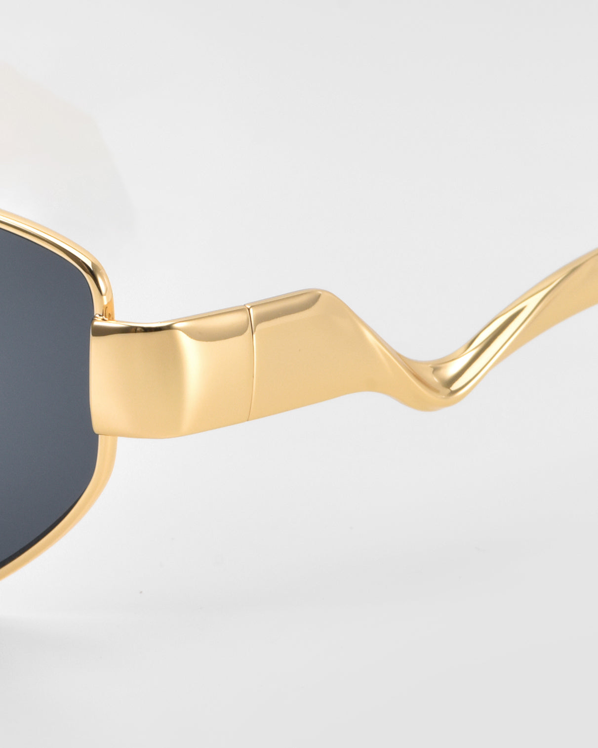 Close-up of For Art's Sake® Abstraction II statement eyewear with a gold geometric metal frame, dark lenses, and wavy sculpted temples, shown against a plain light background.