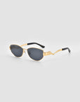 For Art's Sake® Abstraction II sunglasses with gold frames, dark oval lenses, black earpieces, and sculptural zigzag temples, shown on a light gray background.