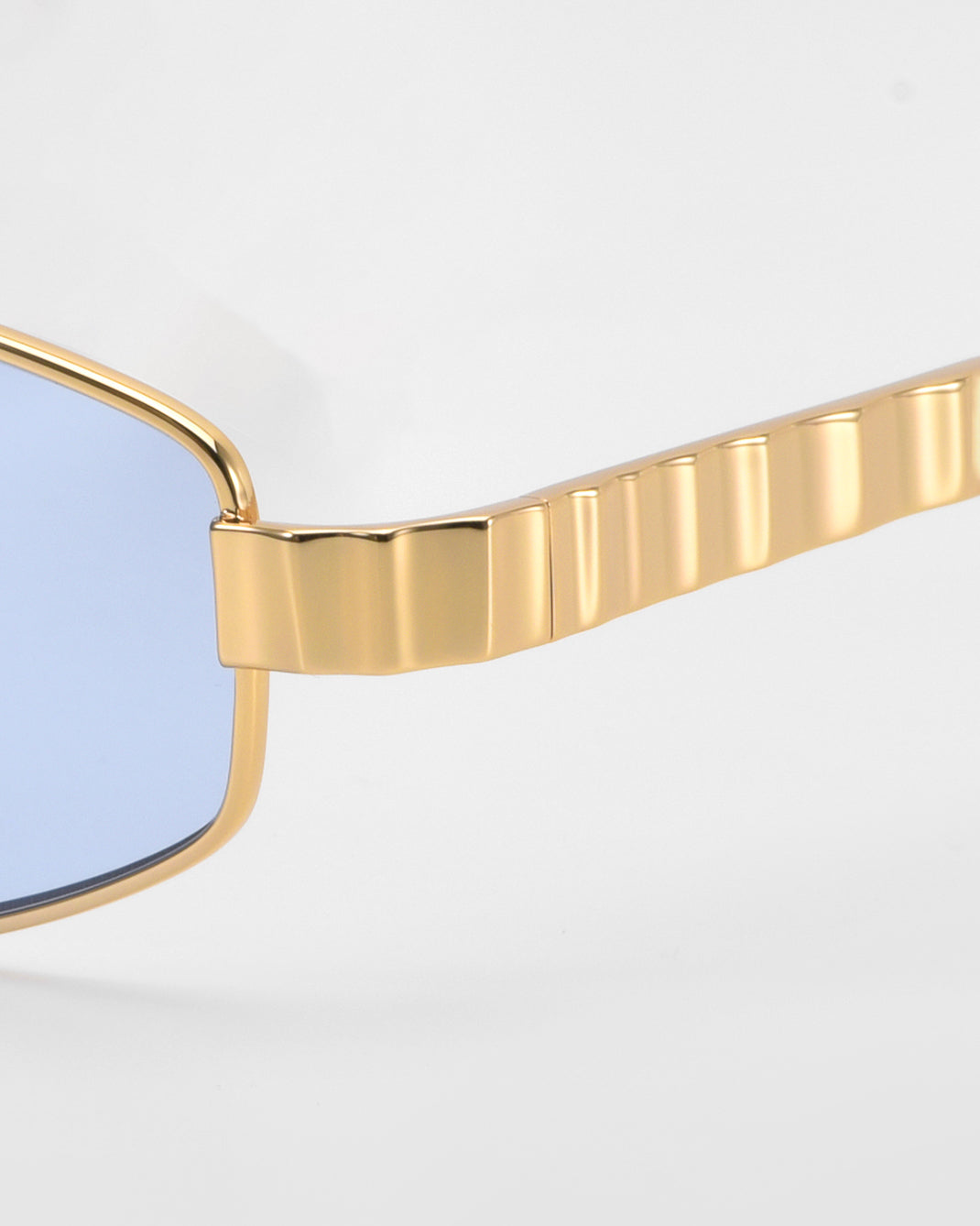 Close-up of For Art's Sake® Mesa I sunglasses with gold metal frames, ridged textured gold arms, and light blue tinted lenses, showcasing the sculptural design against a plain background.