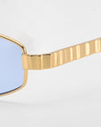 Close-up of For Art's Sake® Mesa I sunglasses with gold metal frames, ridged textured gold arms, and light blue tinted lenses, showcasing the sculptural design against a plain background.