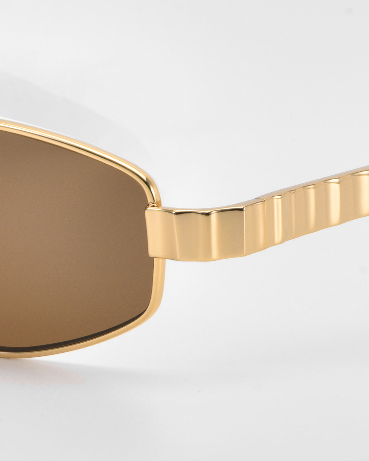 Close-up of For Art's Sake® Mesa I luxury sunglasses with brown-tinted lenses and a gold, textured frame and arm, set against a plain white background.