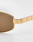 Close-up of For Art's Sake® Mesa I luxury sunglasses with brown-tinted lenses and a gold, textured frame and arm, set against a plain white background.