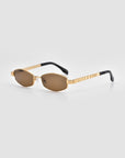 Mesa I sunglasses by For Art's Sake® feature gold oval frames, brown-tinted lenses, and black temple tips. These sculptural eyewear pieces are shown on a light gray background.
