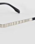 Close-up of the Mesa I temple arm by For Art’s Sake®, showcasing metallic ripple texture and black tips against a plain light gray background for a refined, luxurious feel.