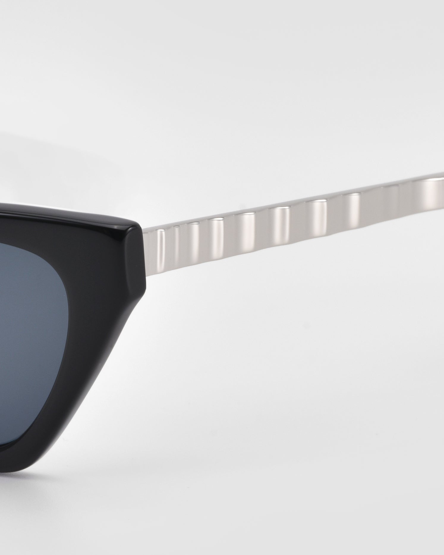 Close-up of For Art's Sake® Mesa II sunglasses with a thick, glossy acetate frame and a silver, textured metal arm against a plain white background.