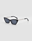 The For Art's Sake® Mesa II sunglasses are luxury cat-eye shades with dark lenses and silver metallic arms, shown on a light gray background.