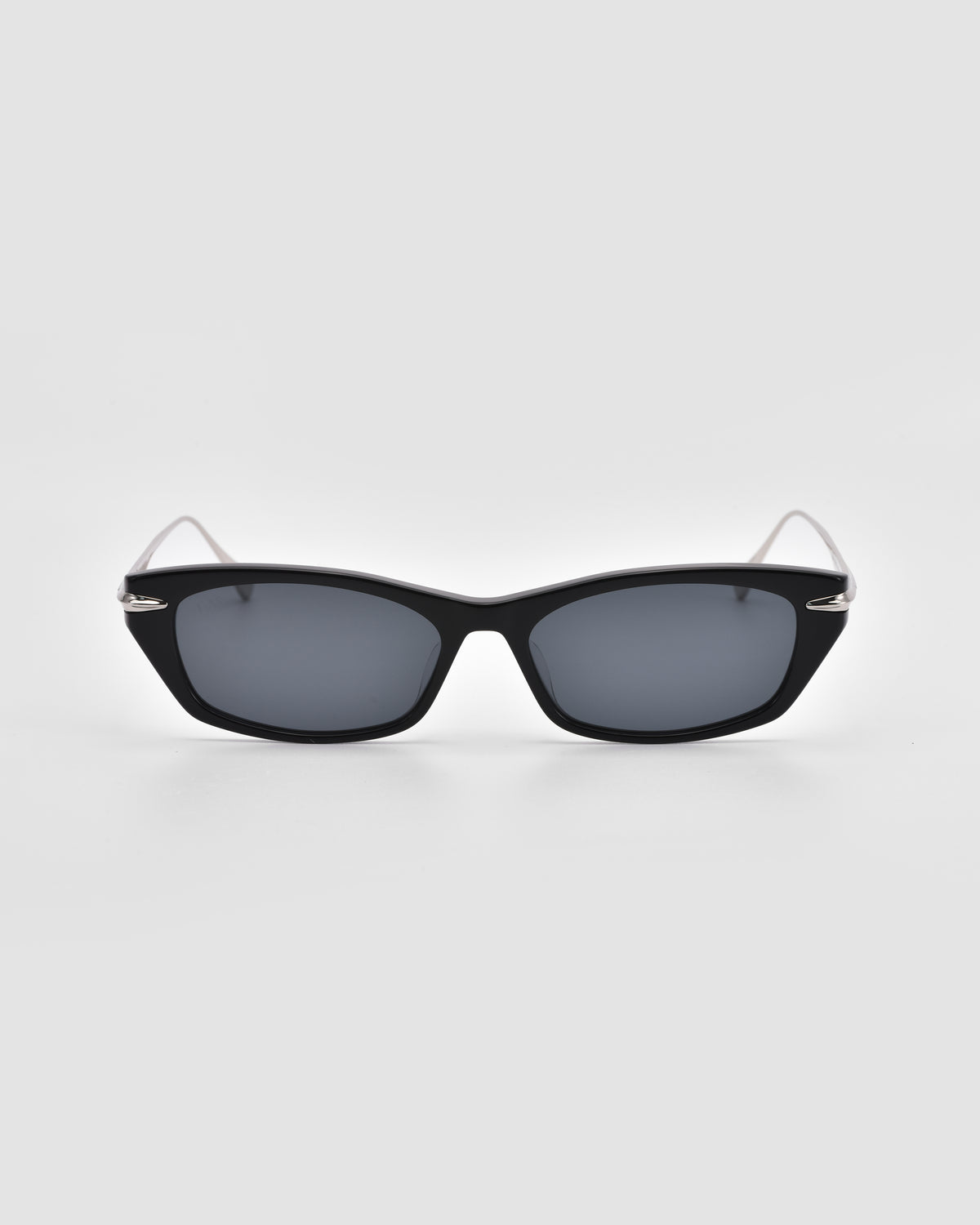 For Art’s Sake® Marisol I: Black cat-eye sunglasses with dark lenses, acetate frame, and thin silver arms, displayed on a plain light gray background facing forward for timeless sun protection.