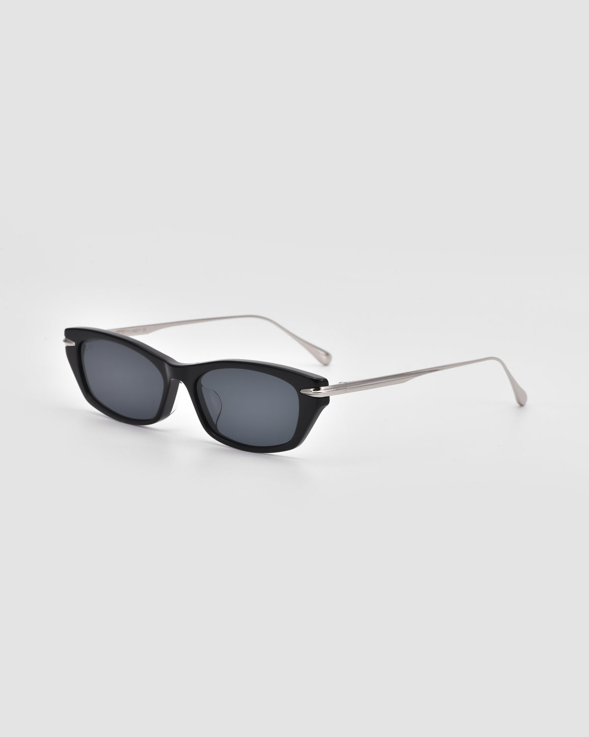 The Marisol I by For Art’s Sake® features black rectangular acetate frames, dark lenses, and slim silver metal arms for stylish sun protection against a light gray background.