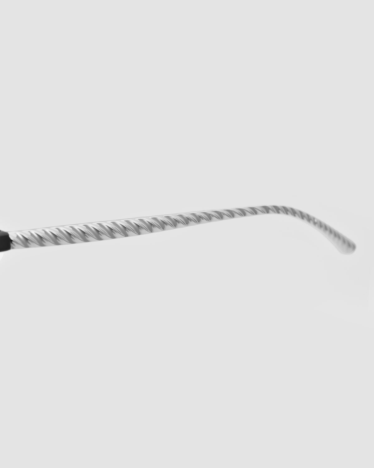 A close-up of the Solana I by For Art’s Sake® highlights its metallic, spiral-designed eyeglasses arm against a plain light gray background—a bold statement piece.