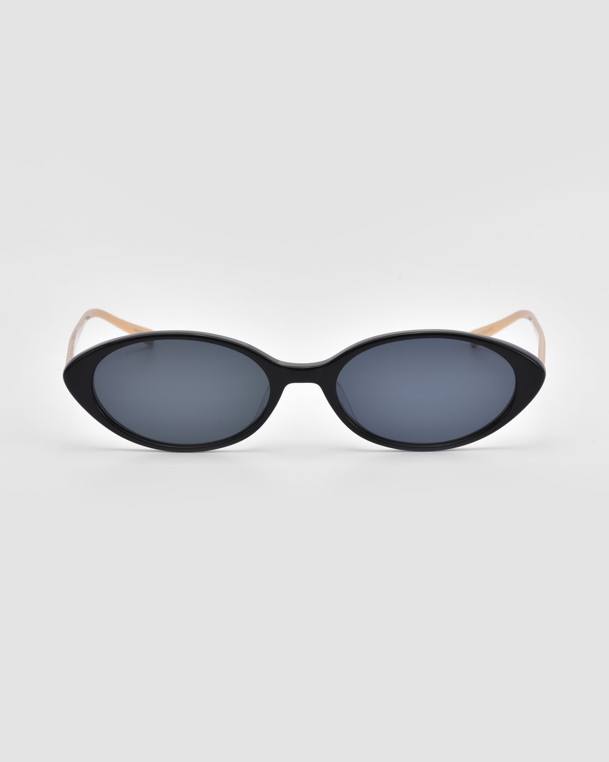 The Solana II by For Art’s Sake® features black cat-eye frames, dark lenses, and thin beige arms, shown here on a plain light gray background.