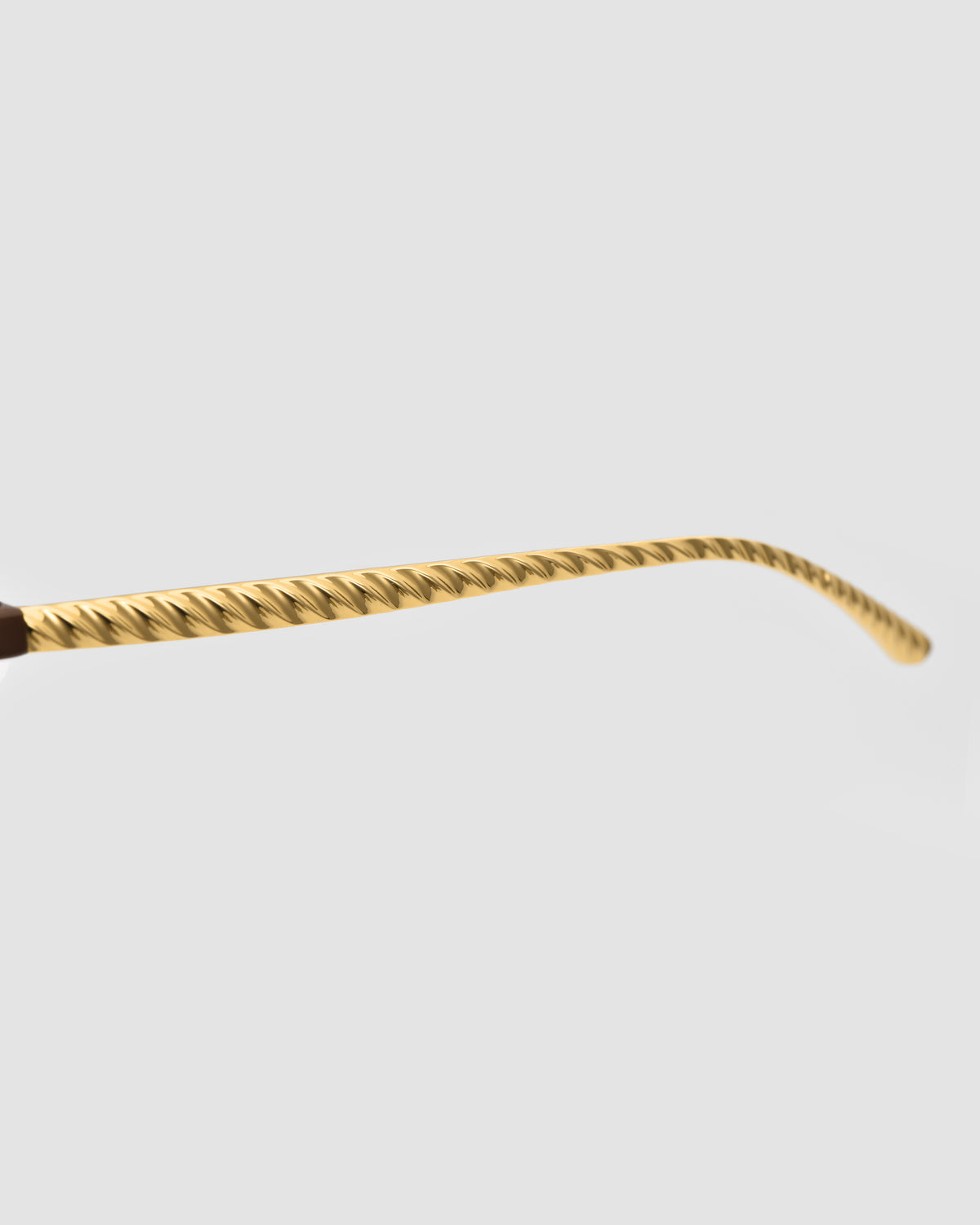 A close-up of the Solana II gold temple arm by For Art’s Sake®, featuring a twisted, textured design inspired by jewellery, set against a plain light gray background.