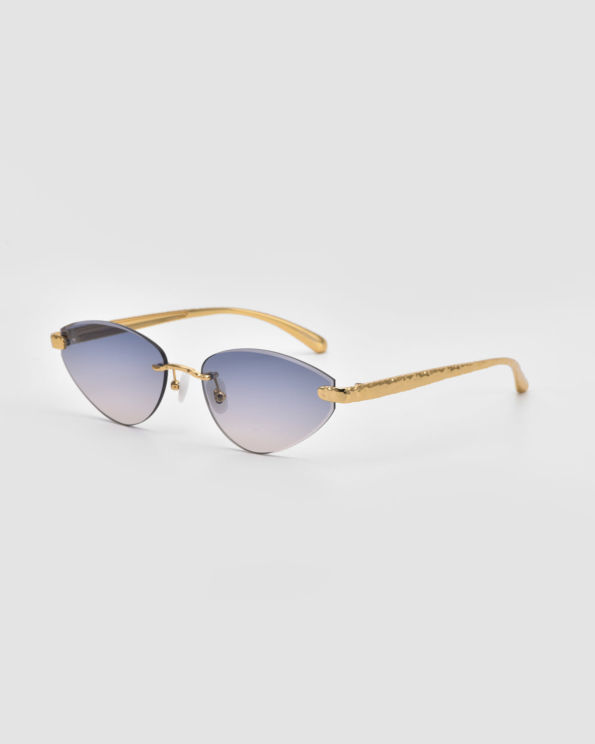 The Shimmer I by For Art’s Sake® features gold frames, blue-tinted cat-eye lenses, thin temples, and gradient bevel-cut lenses—an elegant, jewellery-inspired look on a plain gray background.