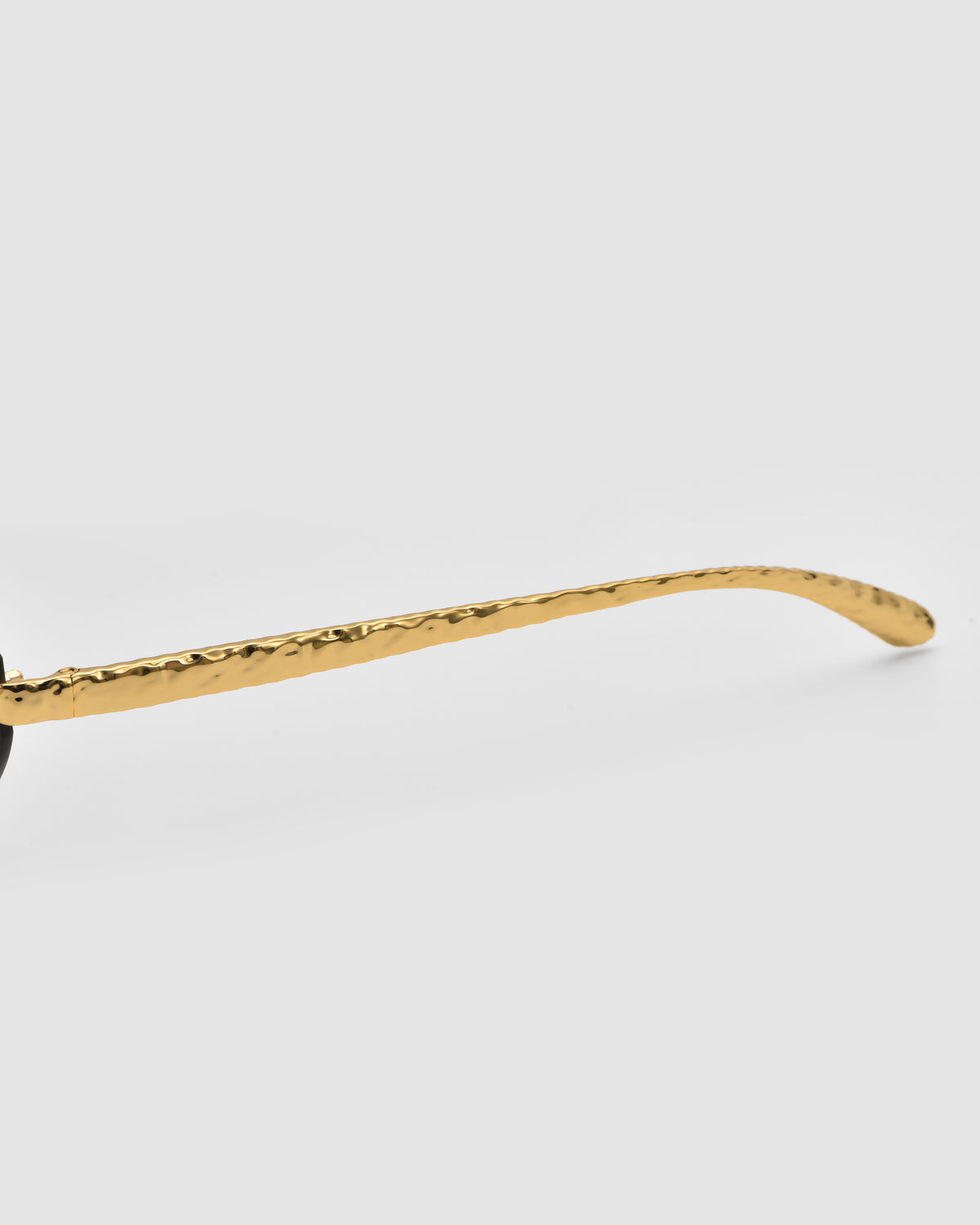 Close-up of Shimmer I by For Art’s Sake®: a gold, textured eyeglass arm with jewellery-inspired temples on a plain light gray background.