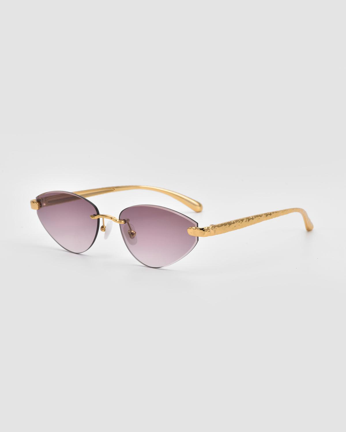Shimmer I by For Art’s Sake®: gold-framed cat-eye sunglasses with bevel-cut purple tinted lenses and textured arms, shown on a light gray background.