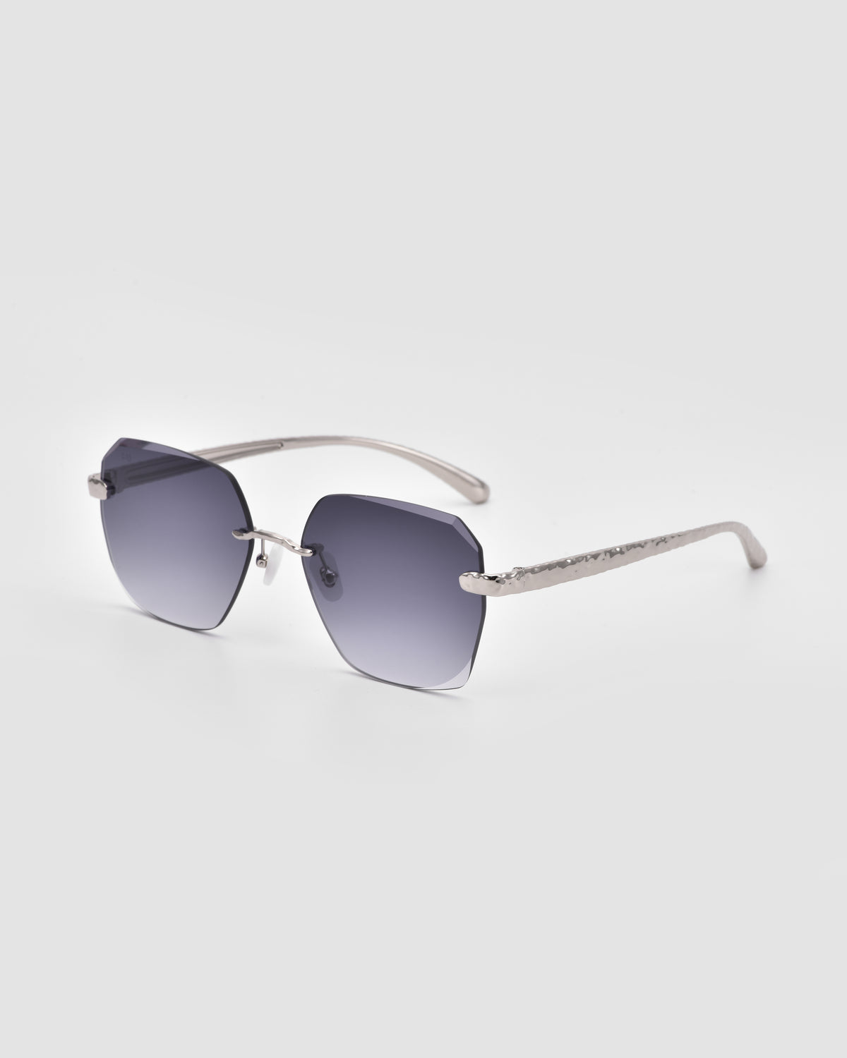 Shimmer II by For Art’s Sake®: Rimless sunglasses with bevel-cut rectangular gray gradient lenses and slim silver metal arms with jewellery-inspired temples, shown on a light gray background.