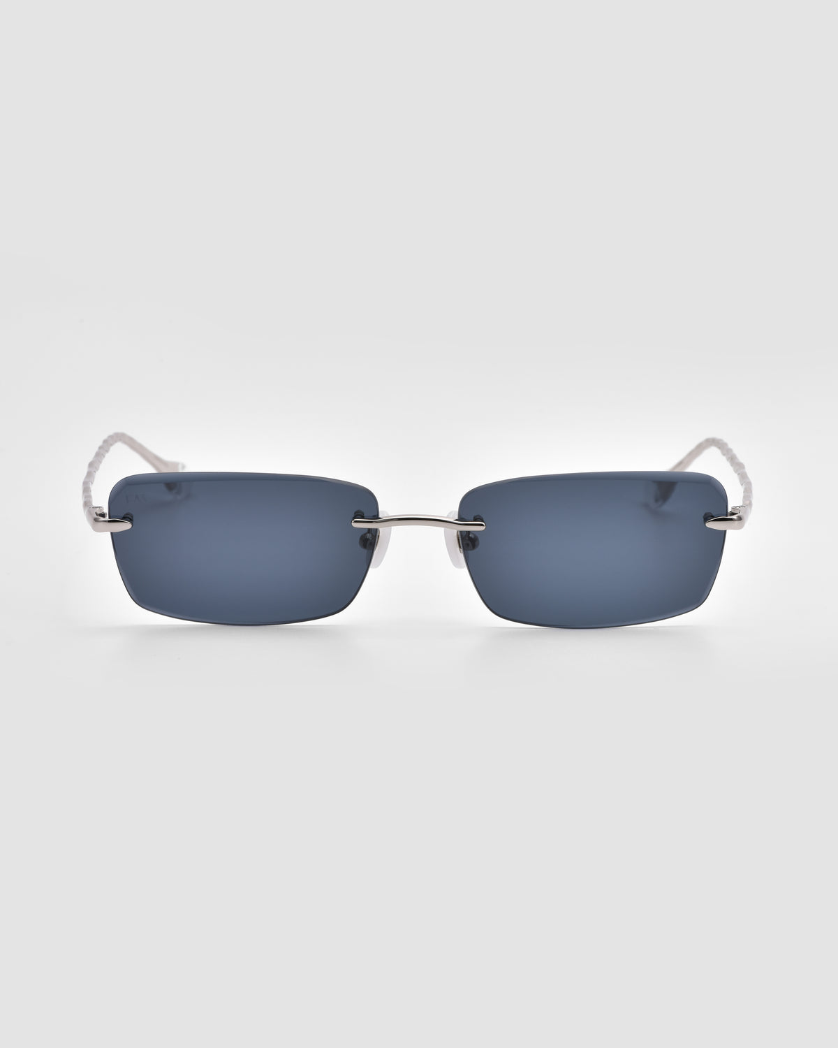 Rectangular, rimless For Art’s Sake® Sol I sunglasses with translucent jewel frame, dark blue lenses, and slim silver arms with sculpted nylon tips. Shown on a light gray background; part of the Sol State collection.
