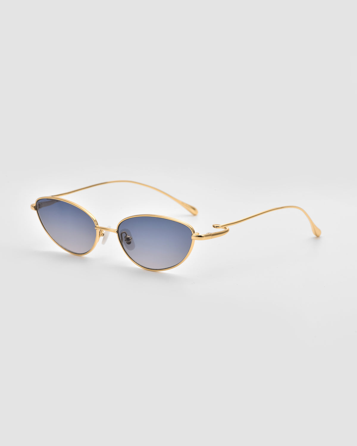 The Ozanne I from For Art’s Sake® features gold-framed, jewelry-inspired sunglasses with oval blue-tinted lenses, shown on a light gray background to highlight their sculptural design.