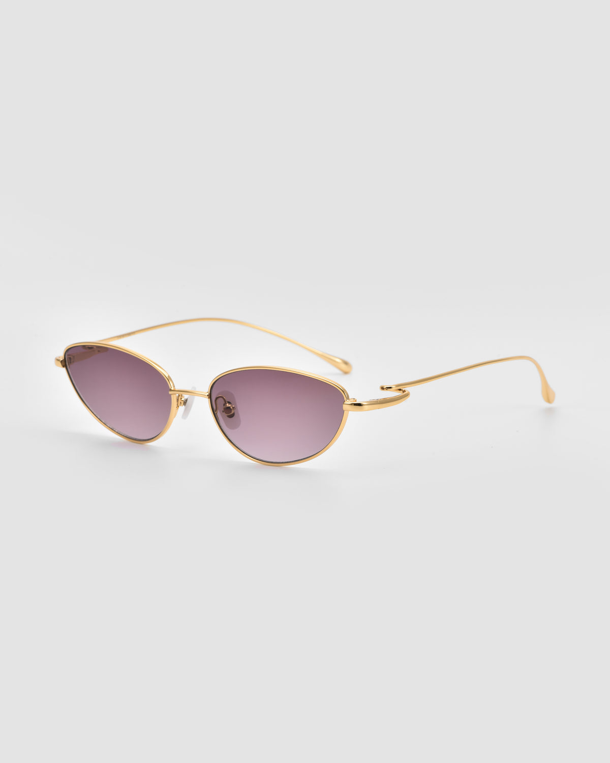 Ozanne I by For Art’s Sake®: Gold-framed cat-eye sunglasses with purple-tinted lenses, shown on a light gray background, highlighting the sculptural looped temples and jewellery-inspired design.