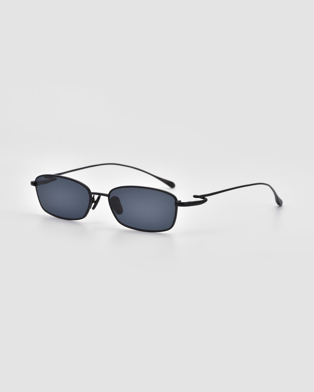 Ozanne II by For Art’s Sake®: black rectangular sunglasses with thin frames, dark lenses, and sculptural looped temples, shown on a light gray background.