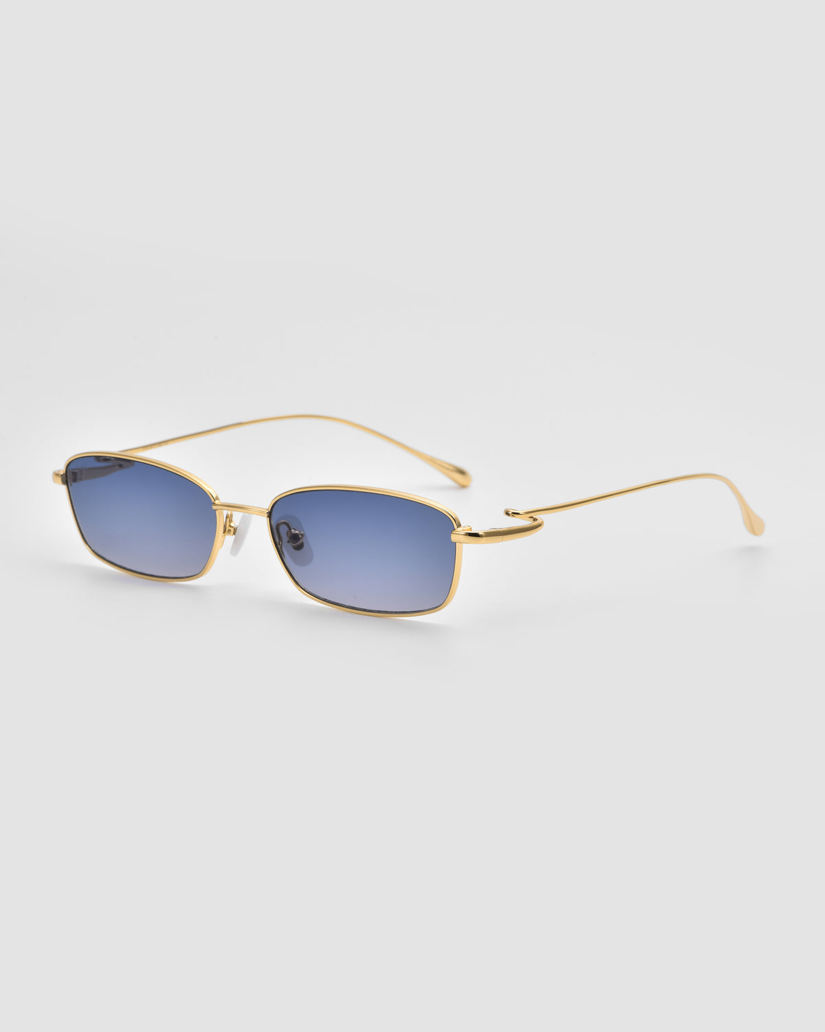Ozanne II by For Art’s Sake®: Gold-framed rectangular sunglasses with blue-tinted lenses and sculptural temples. Lightweight with thin, curved arms, shown on a light gray background.