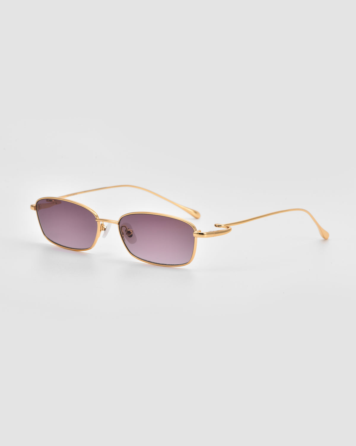 Ozanne II by For Art’s Sake®: Gold-framed, lightweight sunglasses with rectangular purple-tinted lenses. Slim arms feature sculptural looped temples and gently outward curves, shown on a light gray background.