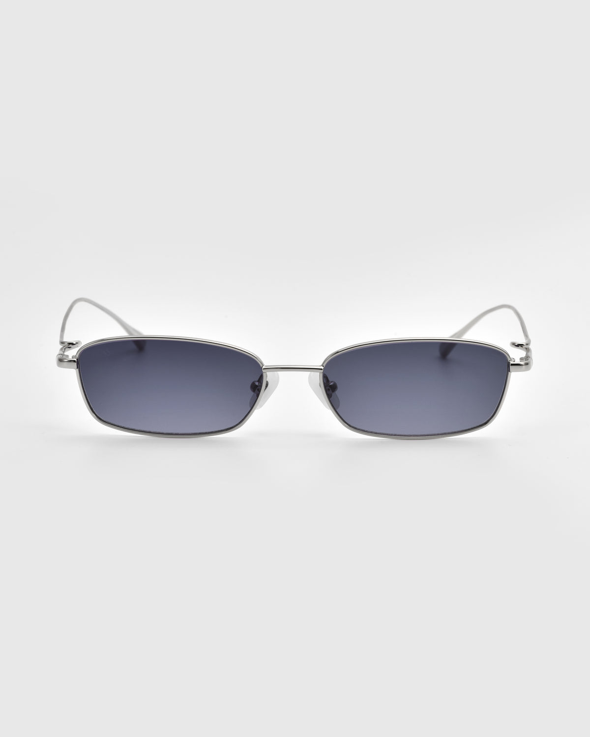 Ozanne II by For Art’s Sake®: Rectangular silver metal sunglasses with sculptural looped temples and dark tinted lenses, displayed on a plain light grey background.