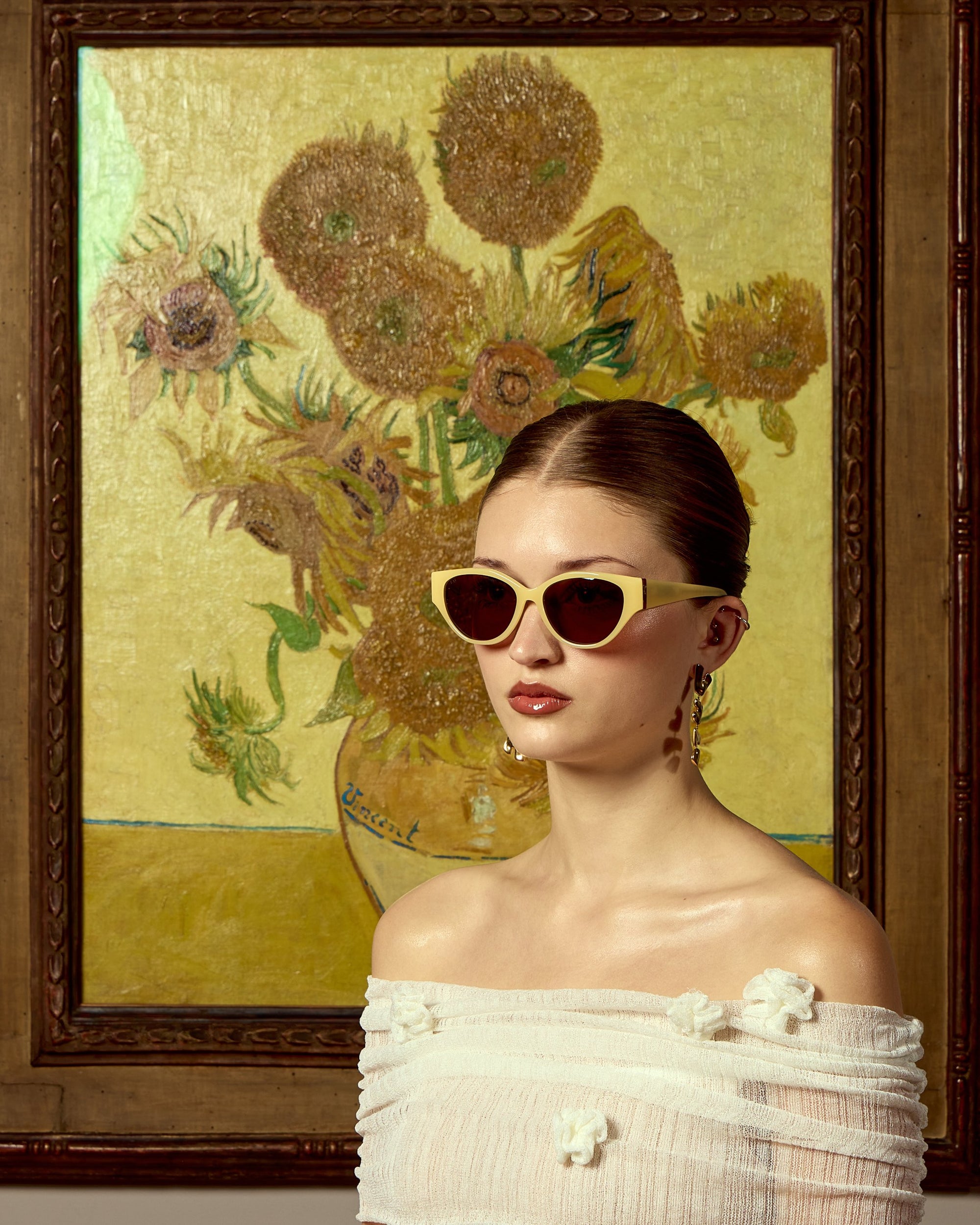 A woman in an off-shoulder white dress and For Art's Sake® cat-eye sunglasses poses before the "Vincent Van Gogh" artwork, elegantly framed on a yellow wall.