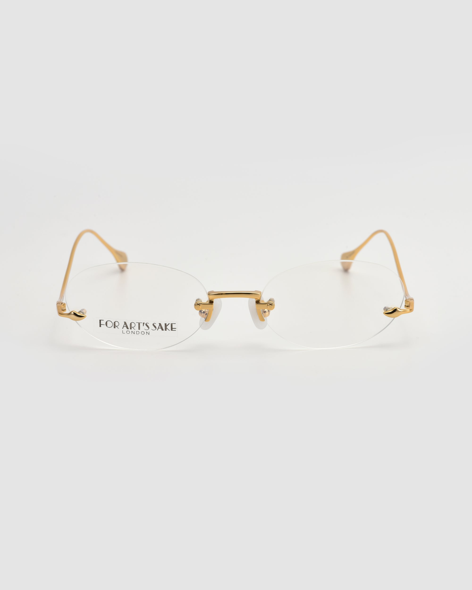 Waver rimless oval glasses by For Art's Sake®, featuring gold metal arms and bridge, are displayed on a plain white background with “For Art’s Sake London” in black on the left lens.