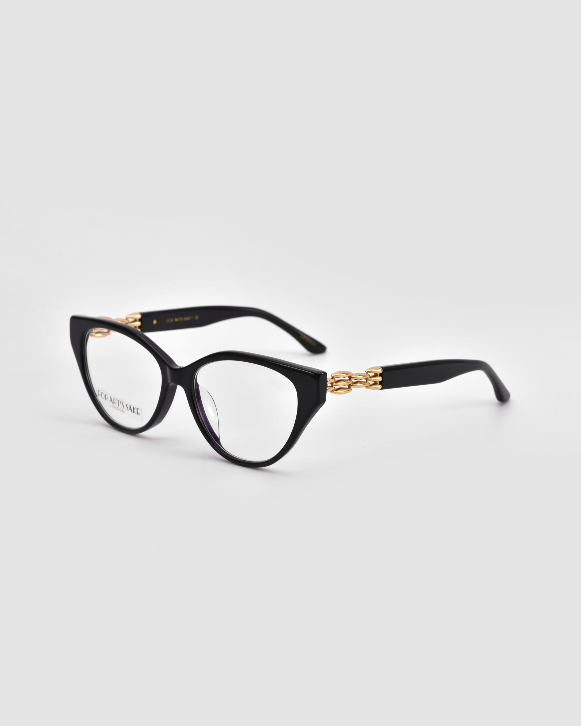 The Act by For Art's Sake®: black cat-eye eyeglasses with gold accents on the arms and a lightweight frame, shown on a light grey background.