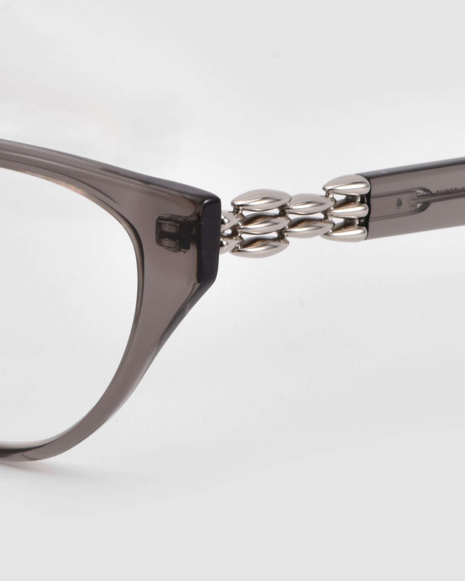 Close-up of For Art&#39;s Sake® The Act eyewear, showcasing its translucent gray frame and silver bead detailing on the temple hinge, set against a plain white background.