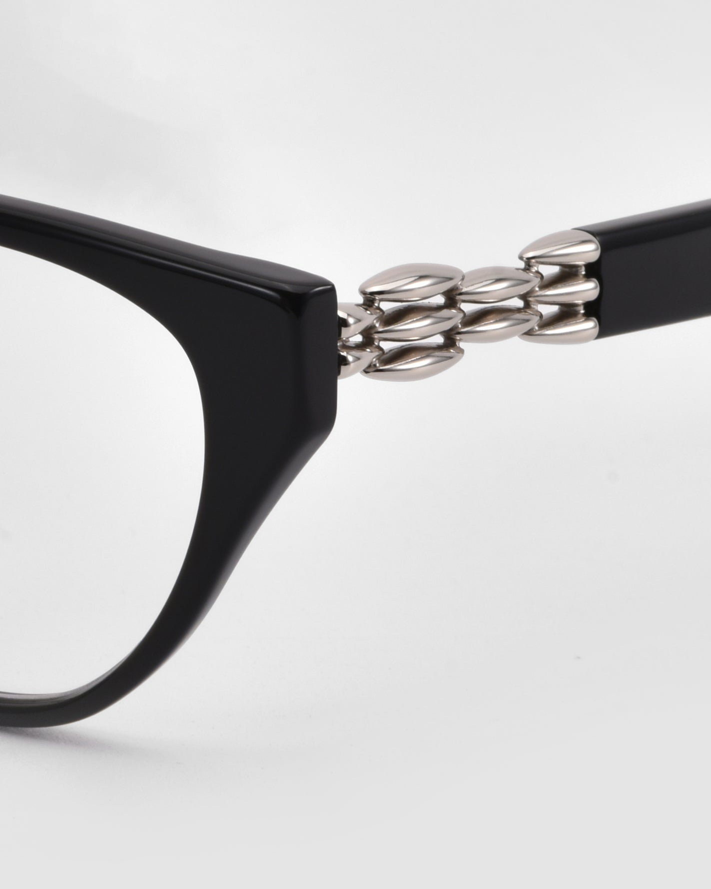 Close-up of The Act by For Art&#39;s Sake®—black sculptural eyewear with unique interlocking silver oval hinge detail—set against a plain white background.