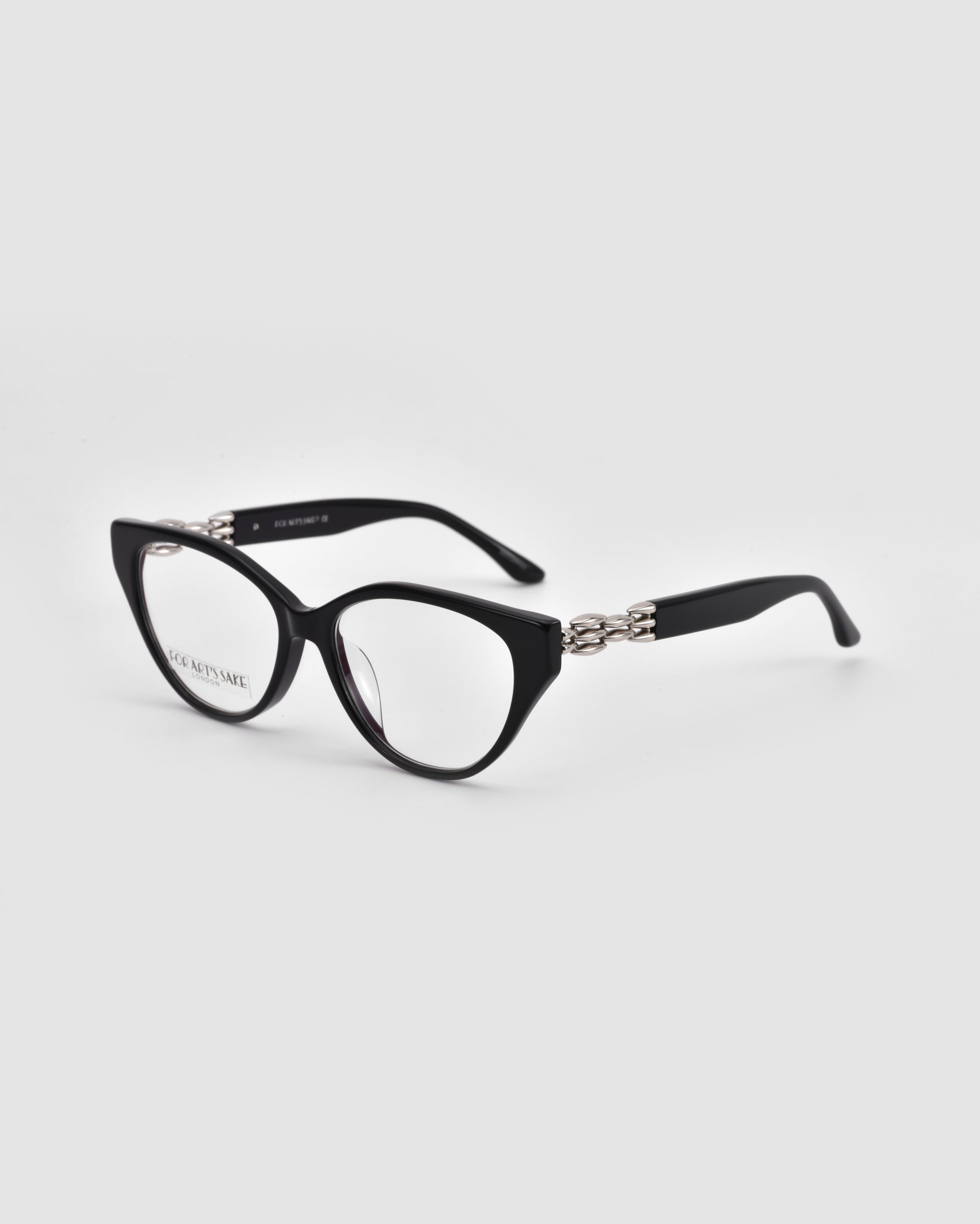 The Act by For Art's Sake® features black cat-eye eyeglasses with silver chain detailing on the temples, offering a minimalist yet chic look. Displayed against a light gray background.