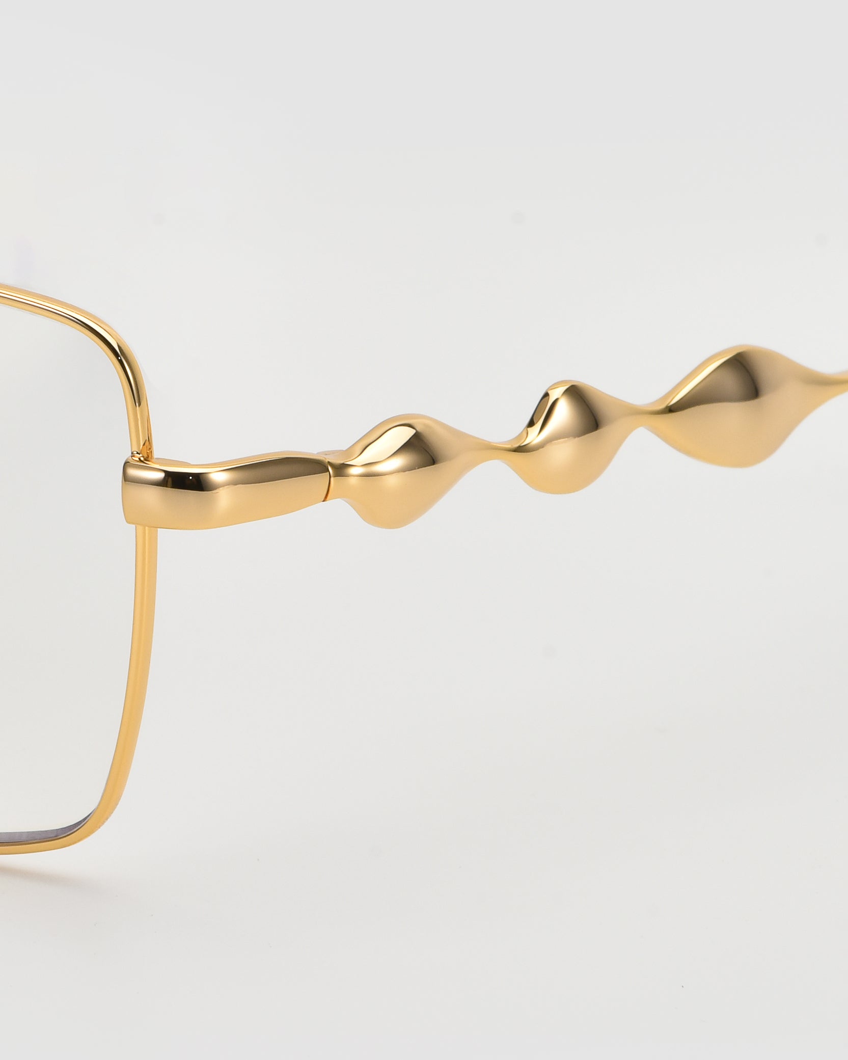 Close-up of For Art&#39;s Sake® Fluid gold eyeglasses with a soft-square silhouette and unique, wavy sculpted arms. The thin metallic frame highlights undulating temples, showcasing the brand’s signature fluid optical design against a white background.