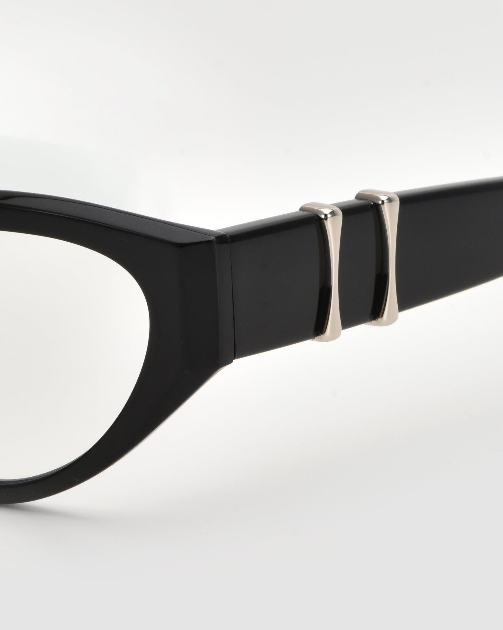 Close-up of the temple of Halo(X) black eyeglasses by For Art&#39;s Sake®, showing a sculptural acetate frame and two silver metallic accents on the arm, set against a white background.