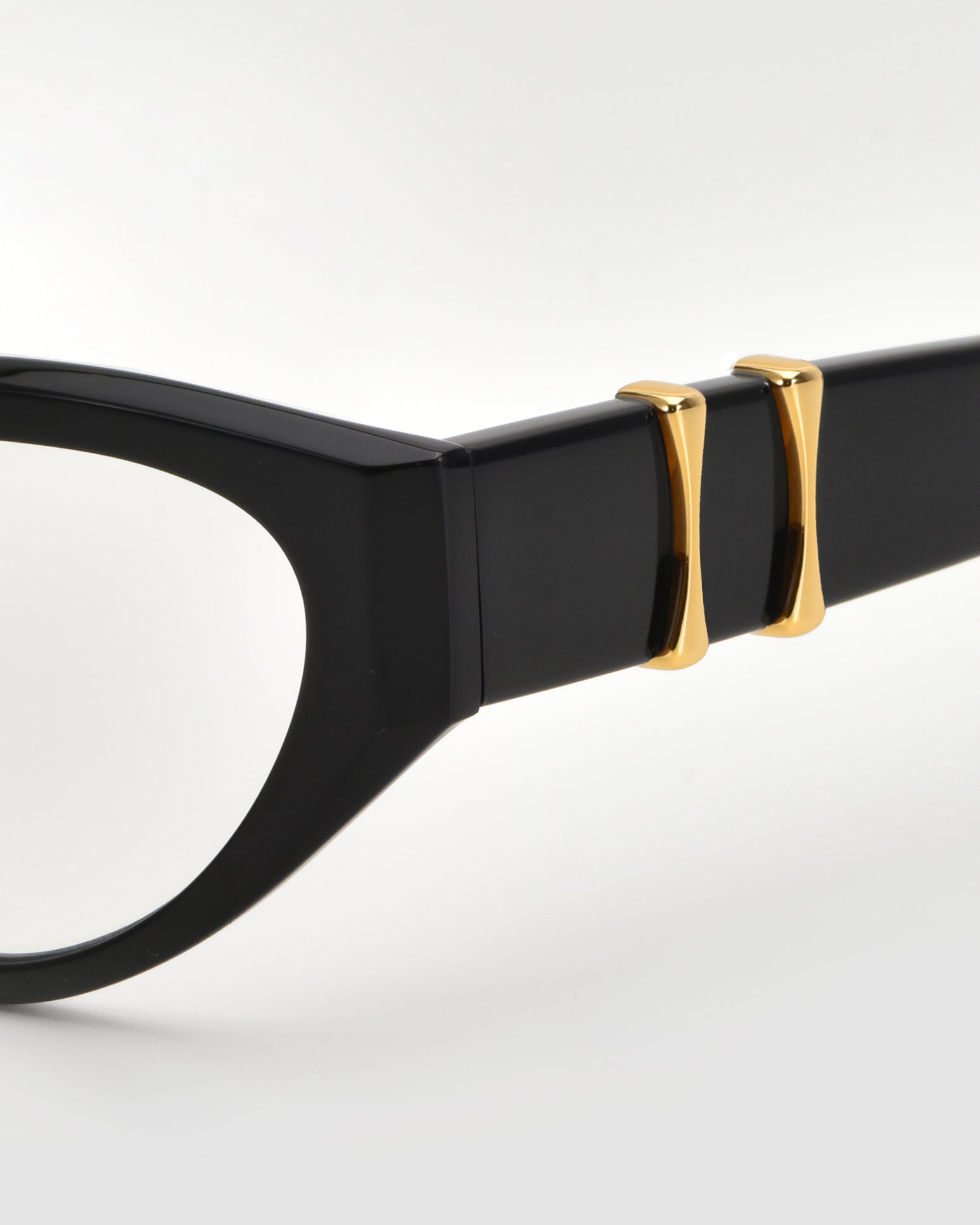 Close-up of the Halo(X) sculptural acetate frames by For Art&#39;s Sake® in classic black, showcasing two gold 3D temple embellishments near the hinge against a plain, light background.