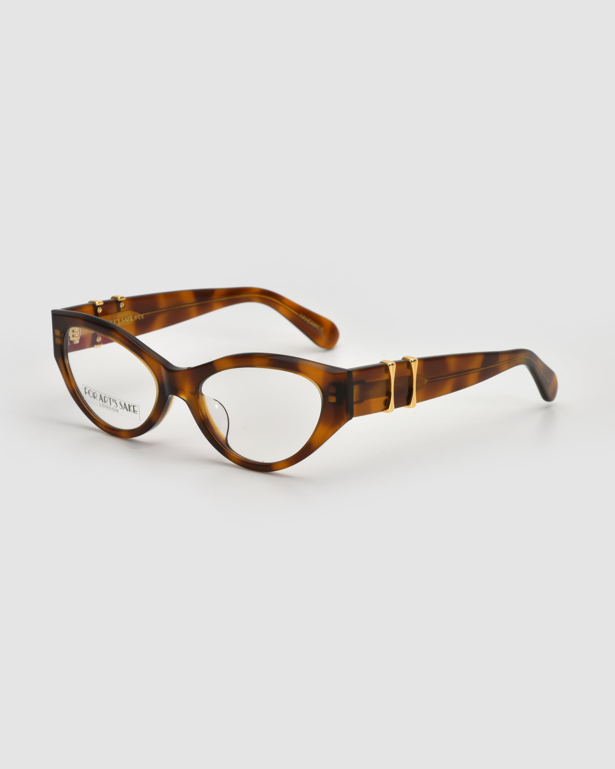 The Halo(X) by For Art's Sake® are brown tortoiseshell cat-eye eyeglasses with gold-accented temples and a sculptural acetate frame, shown on a plain light gray background.