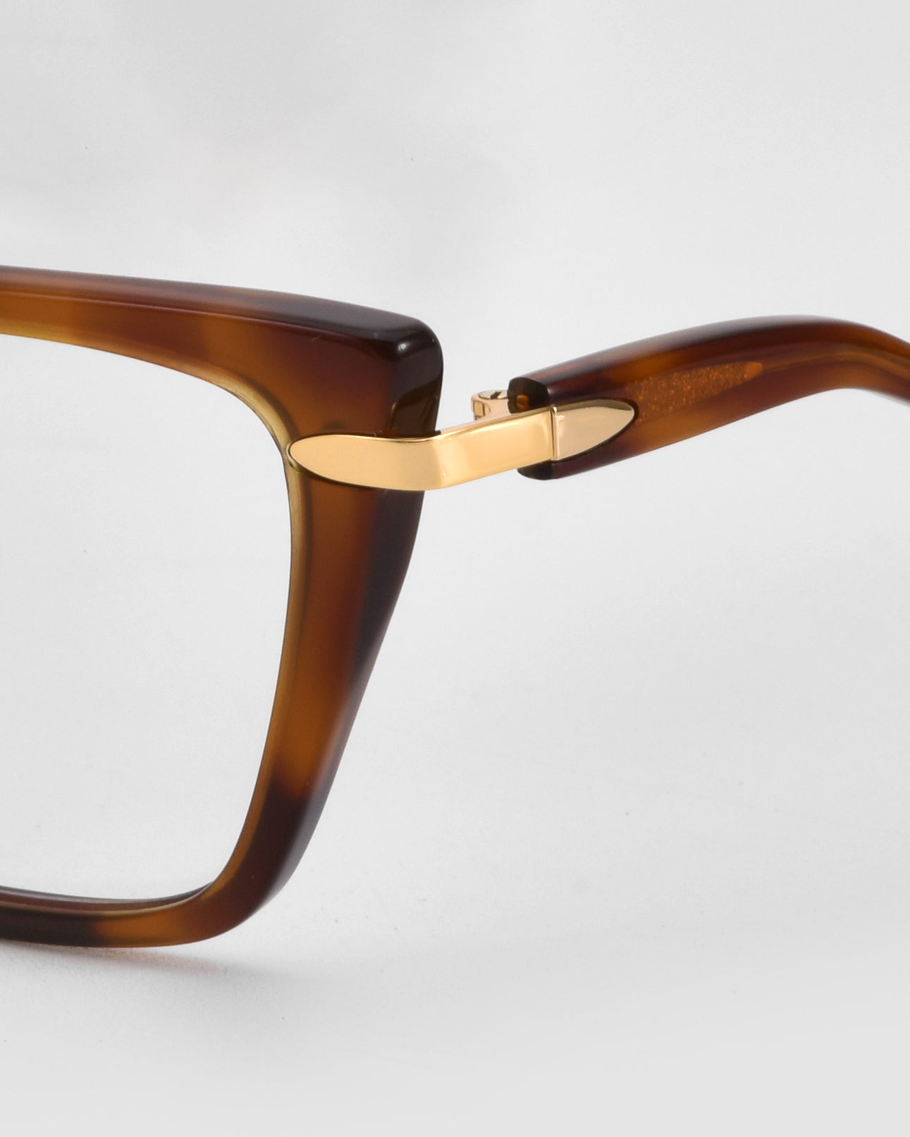 Close-up of the top corner and arm hinge of For Art&#39;s Sake® Motion I brown rectangular frames, featuring gold-tone metal accents at the hinge and acetate temples against a plain light background.