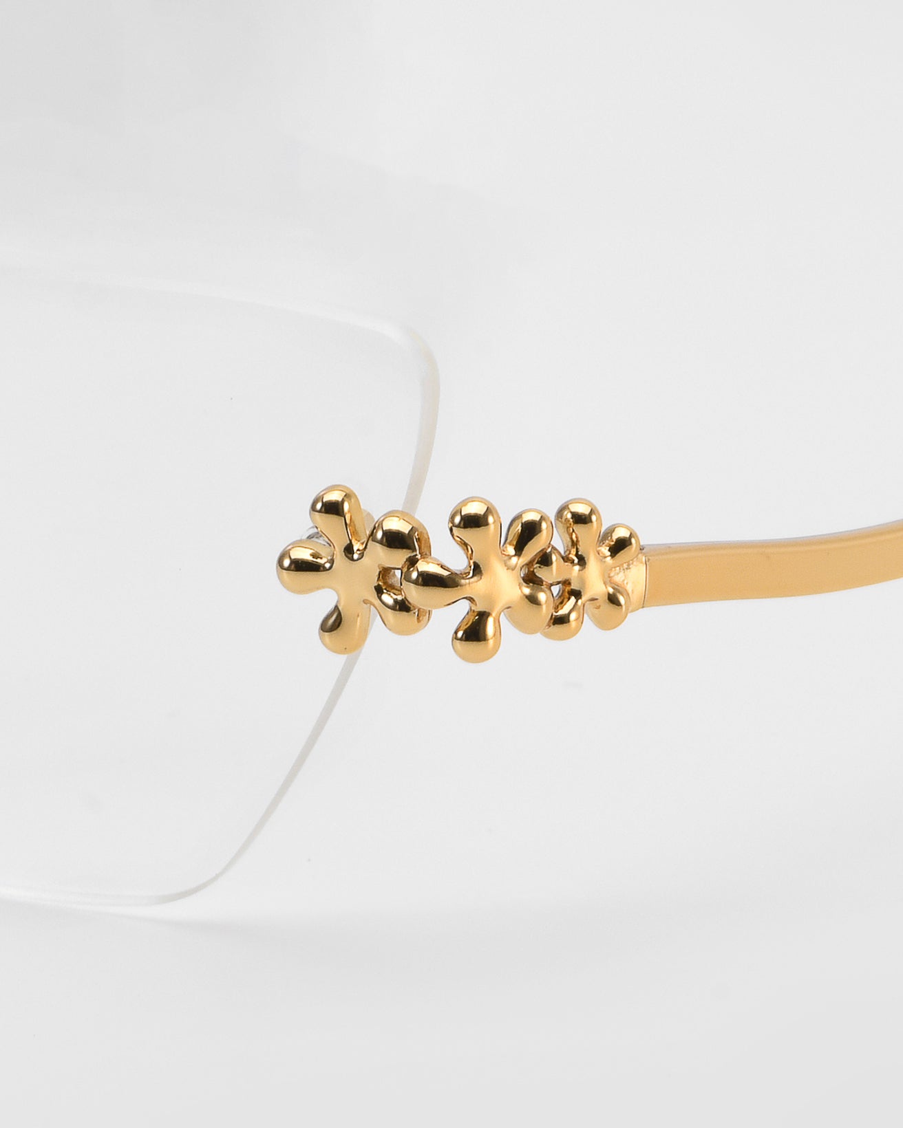 Close-up of For Art's Sake® Ida eyeglasses featuring lightweight frames and gold metal temples with three small flower accents. Set against a plain, light background, the elegant floral optical design is beautifully highlighted.