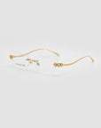 Ida by For Art's Sake®: Rimless, lightweight eyeglasses with clear lenses, a gold nose bridge, and cat-eye temples featuring ornate gold floral designs on the temples and lens corners. Displayed on a plain white background.