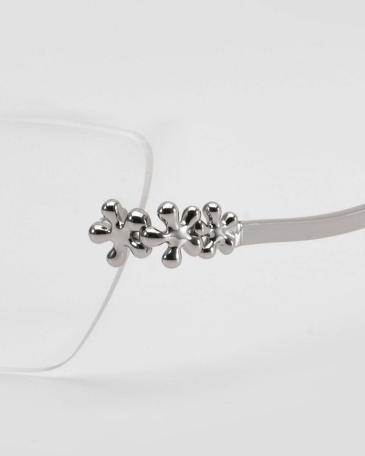 Close-up of For Art's Sake® Ida cat-eye glasses with a metallic, abstract floral design on the temple hinge, set against a white background.