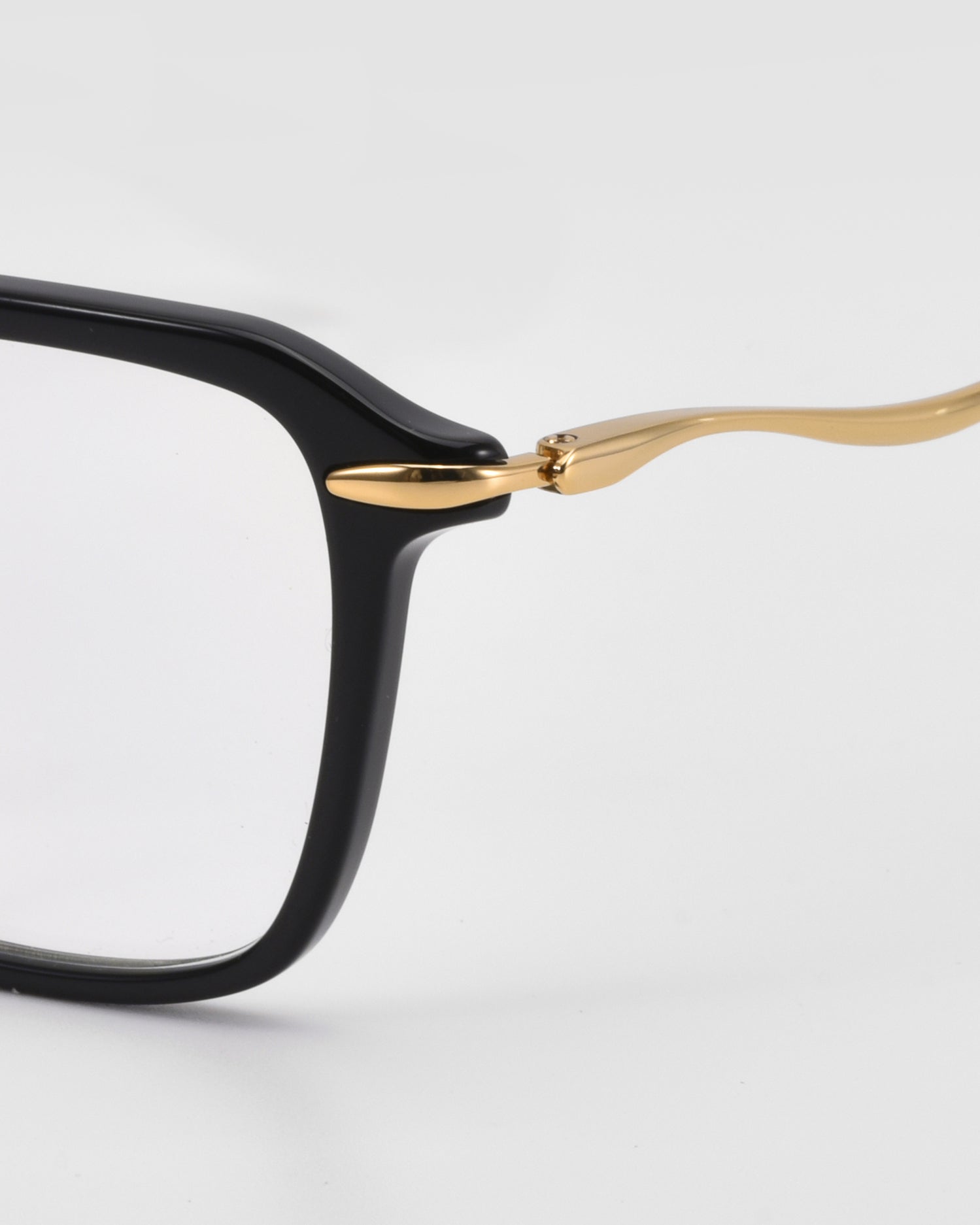 Close-up of the Claudia eyeglass frame by For Art's Sake® featuring black acetate, sculpted temples, and a gold metal arm, shown against a plain white background.