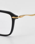 Close-up of the Claudia eyeglass frame by For Art's Sake® featuring black acetate, sculpted temples, and a gold metal arm, shown against a plain white background.