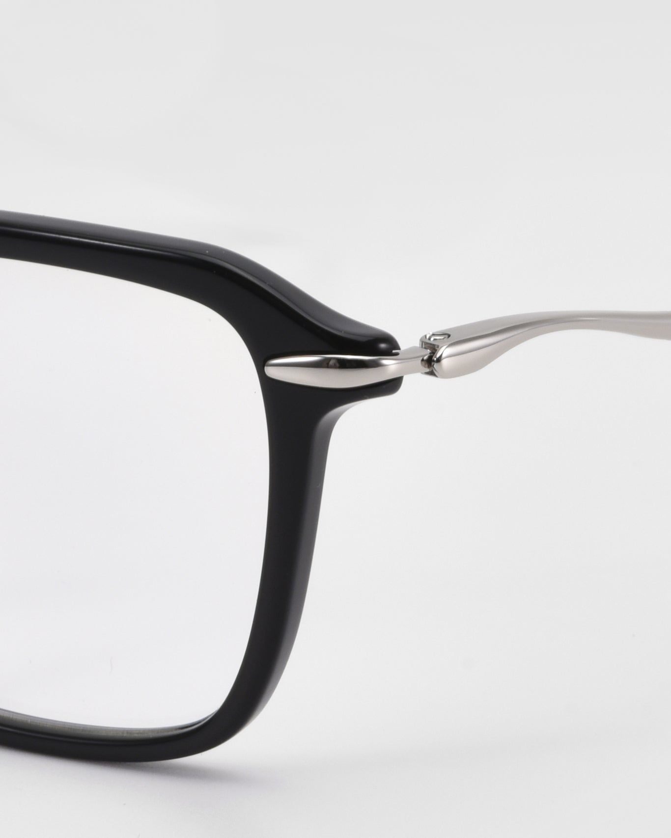 Close-up of the top left corner of For Art’s Sake® Claudia eyeglasses, showing a black rectangular acetate and metal frame with sculpted temples and silver hinge, set against a plain white background.