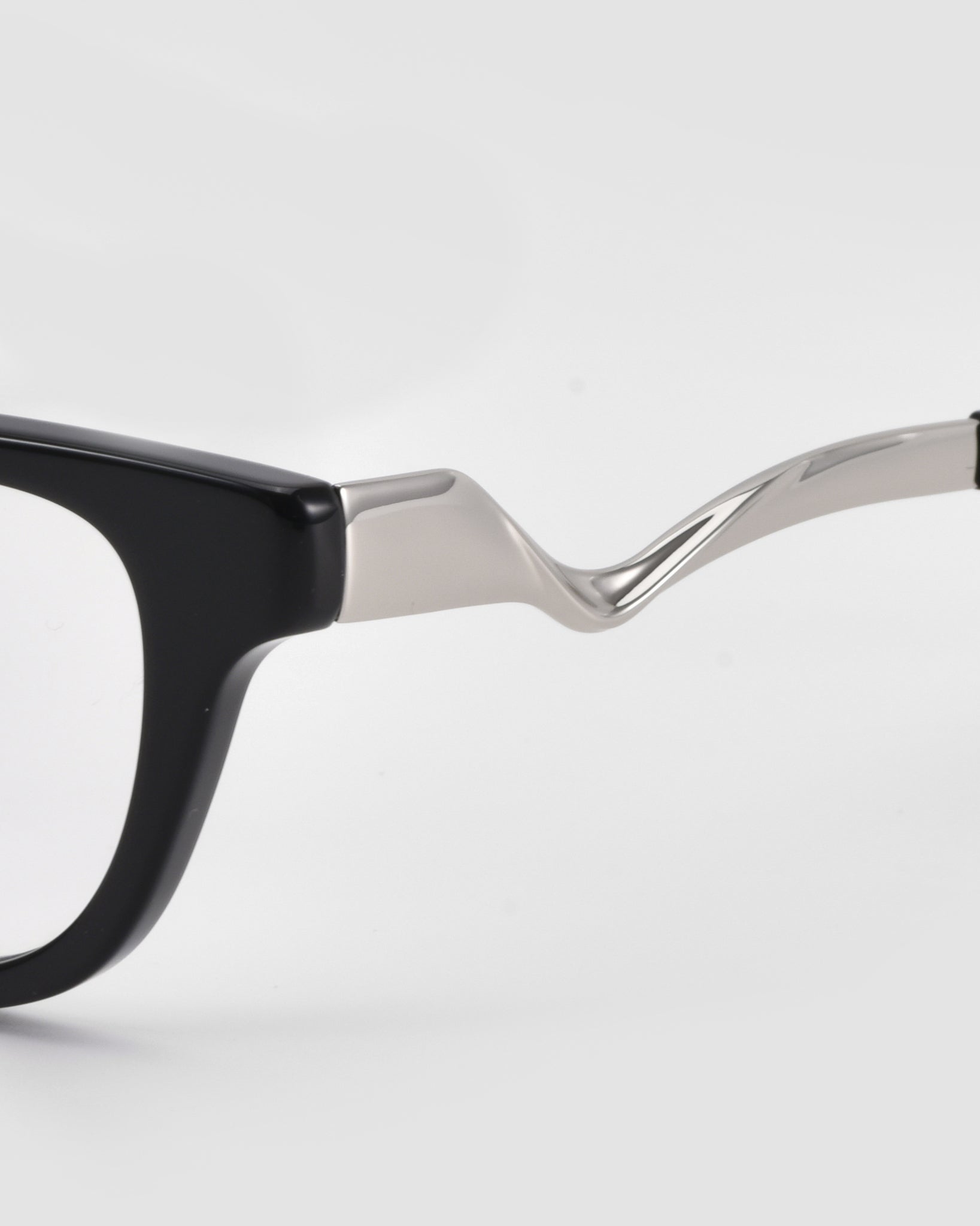 Close-up of the Poppy eyeglasses by For Art's Sake®, featuring a black frame and sculptural, wavy silver metal temples, set against a plain white background.