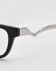 Close-up of the Poppy eyeglasses by For Art's Sake®, featuring a black frame and sculptural, wavy silver metal temples, set against a plain white background.